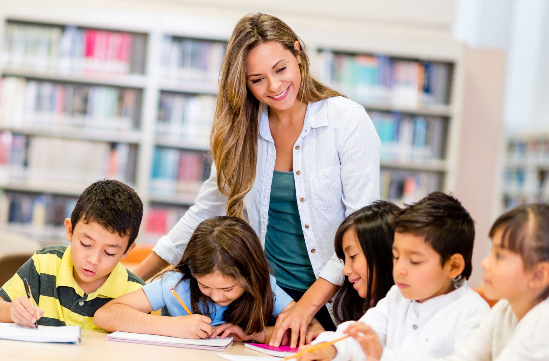 A smiling teacher guiding a group of primary pupils at a library table